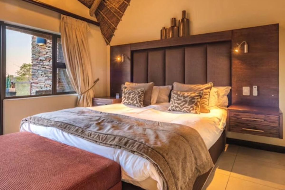 A well-appointed bedroom featuring a high thatched ceiling, custom built-in headboard with integrated bedside tables, and large windows overlooking the exterior.