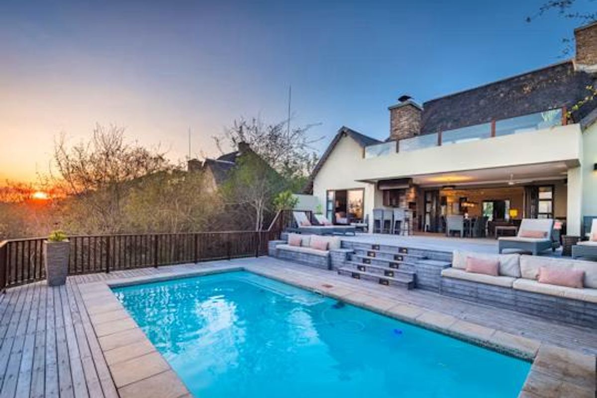A beautifully maintained outdoor pool area featuring extensive timber decking, built-in seating, and a seamless transition to the covered patio and main residence.