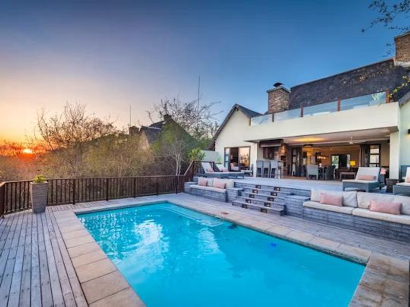 A beautifully maintained outdoor pool area featuring extensive timber decking, built-in seating, and a seamless transition to the covered patio and main residence.