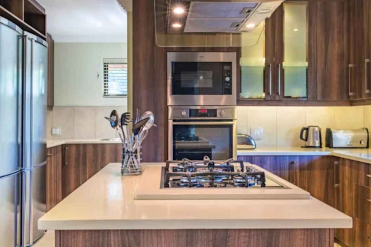 Modern kitchen featuring dark wood cabinetry, stone countertops, a central island with a gas hob, and integrated stainless steel appliances.