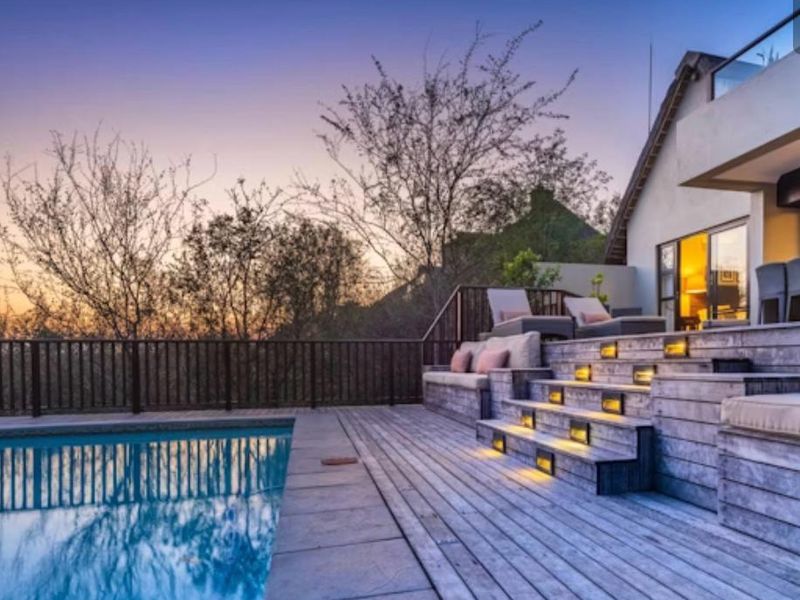 Outdoor pool area featuring extensive timber decking, built-in seating, integrated stair lighting, and a timber balustrade overlooking the landscape.