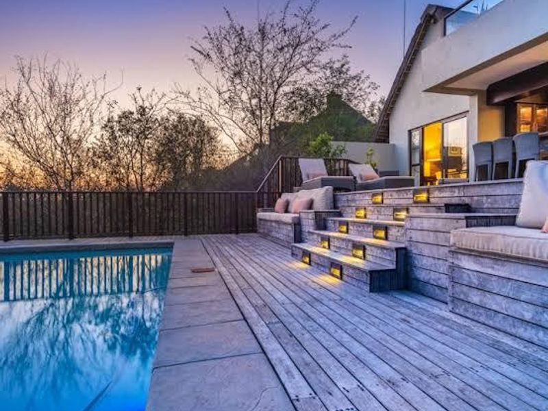 A beautifully lit outdoor pool area featuring tiered timber decking with integrated seating and recessed lighting, perfect for evening relaxation.