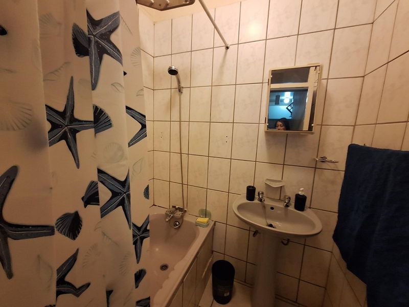 A compact bathroom featuring a pedestal sink, bathtub with shower mixer, and wall-mounted medicine cabinet, finished with dated ceramic wall tiles.
