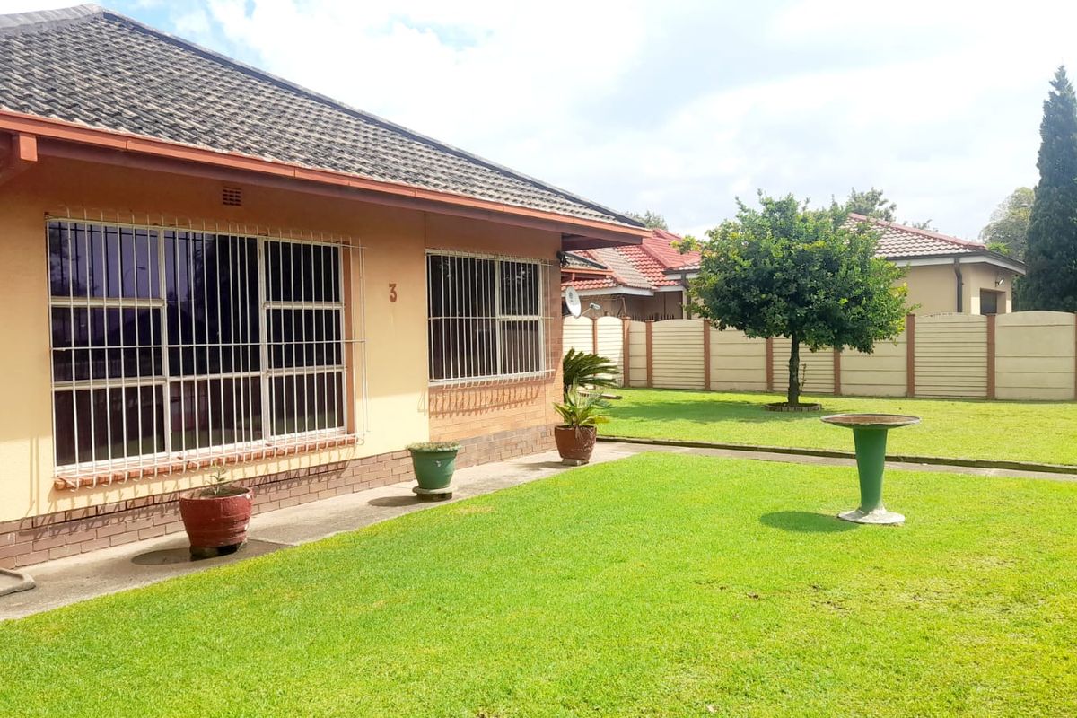 Rear view of the house featuring a well-maintained lawn, concrete walkway, and secure window bars, enclosed by a precast boundary wall.