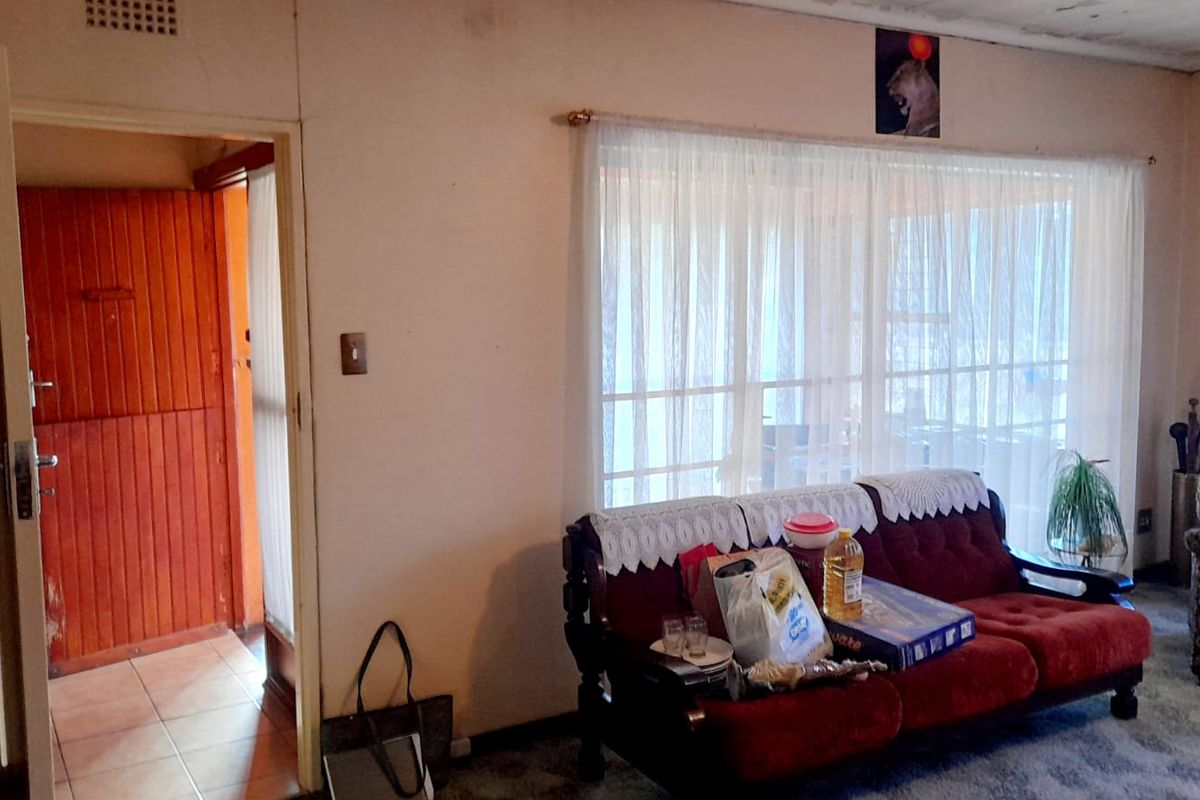 A living room area featuring carpeted flooring and a doorway leading to a tiled hallway with a timber door.