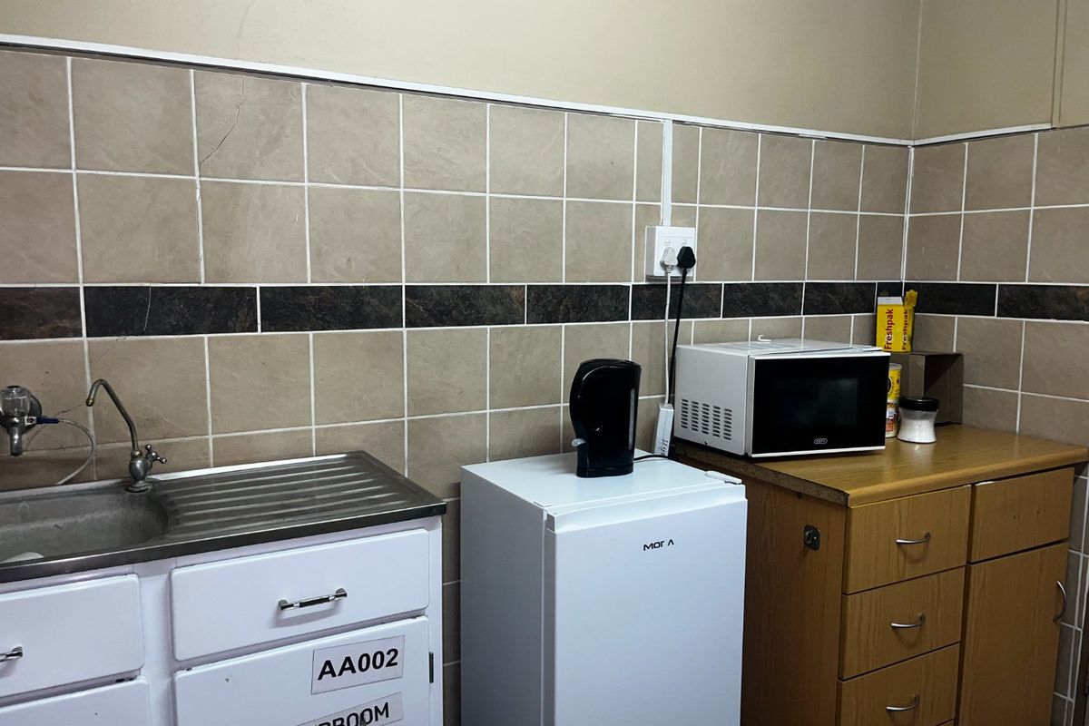 A functional kitchenette area featuring a stainless steel sink, tiled backsplash, and built-in cabinetry, suitable for office or utility use.
