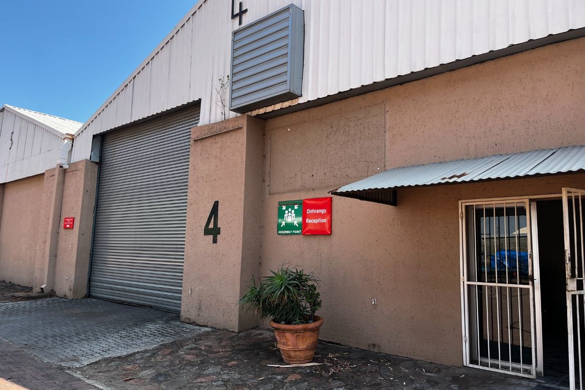 Commercial warehouse unit featuring a large roller shutter door, pedestrian entrance with security gate, and industrial metal roofing.