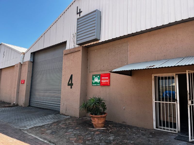 Commercial warehouse unit featuring a large roller shutter door, pedestrian entrance with security gate, and industrial metal roofing.