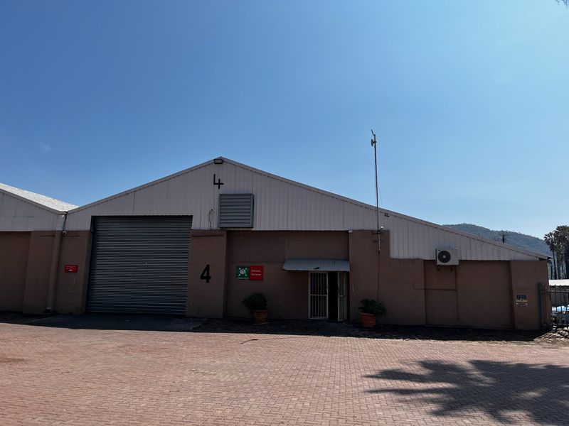 Front elevation of a commercial warehouse unit featuring a large roller shutter door, metal roofing, and paved access area.