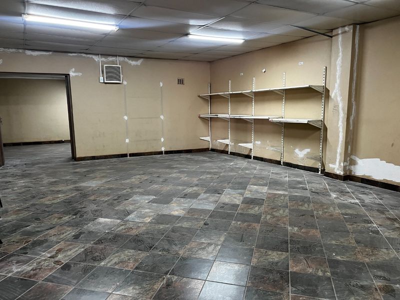 An empty commercial utility or storage space featuring tiled flooring, wall-mounted shelving units, and a drop ceiling with fluorescent lighting.