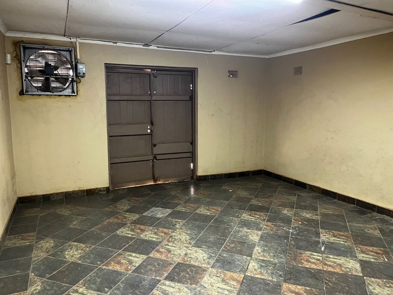 An empty utility or storage space featuring industrial ventilation, tiled flooring, and double timber access doors.
