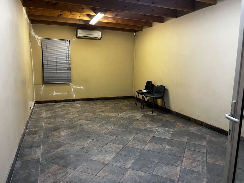 A functional office space featuring exposed timber ceiling beams, tiled flooring, and a wall-mounted air conditioning unit, requiring minor cosmetic wall repairs.