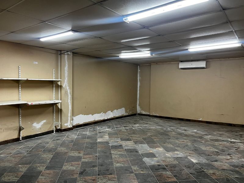 An empty commercial utility or storage space featuring slate tile flooring, suspended ceiling, and wall-mounted air conditioning unit.