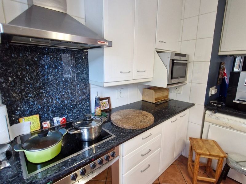 A functional kitchen featuring granite countertops, built-in oven, electric cooktop, stainless steel extractor fan, and white cabinetry with tiled flooring.