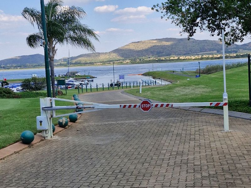 A view of the property entrance featuring a security boom gate, paved driveway, and landscaped grounds overlooking a scenic lake and mountain landscape.