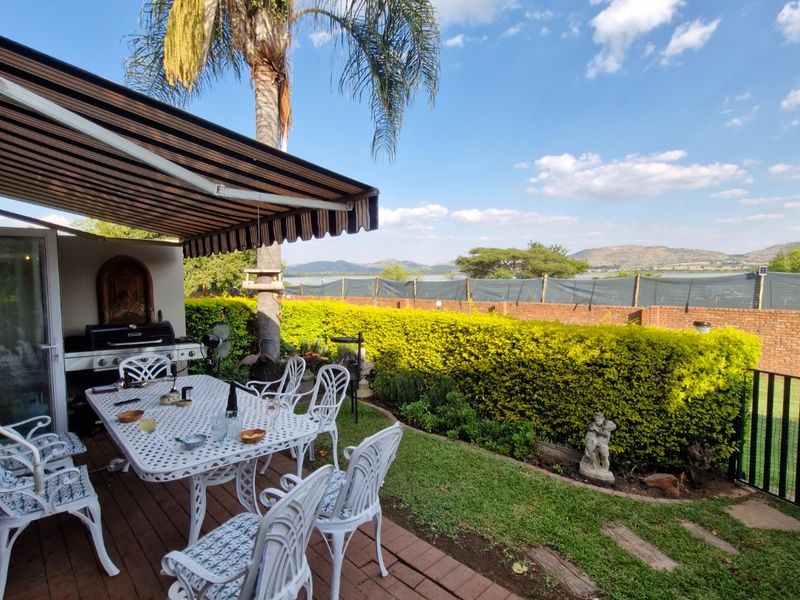 Covered brick-paved patio featuring a retractable awning, overlooking a landscaped garden with mature palm trees and scenic distant views.