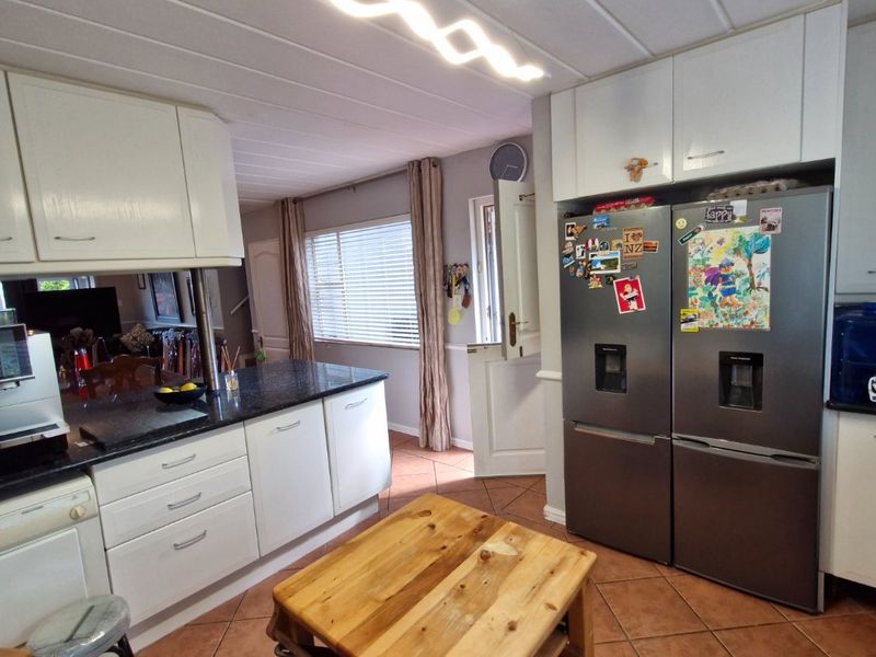 A functional kitchen featuring white cabinetry, granite countertops, and tiled flooring, with a unique dutch door leading to the exterior.