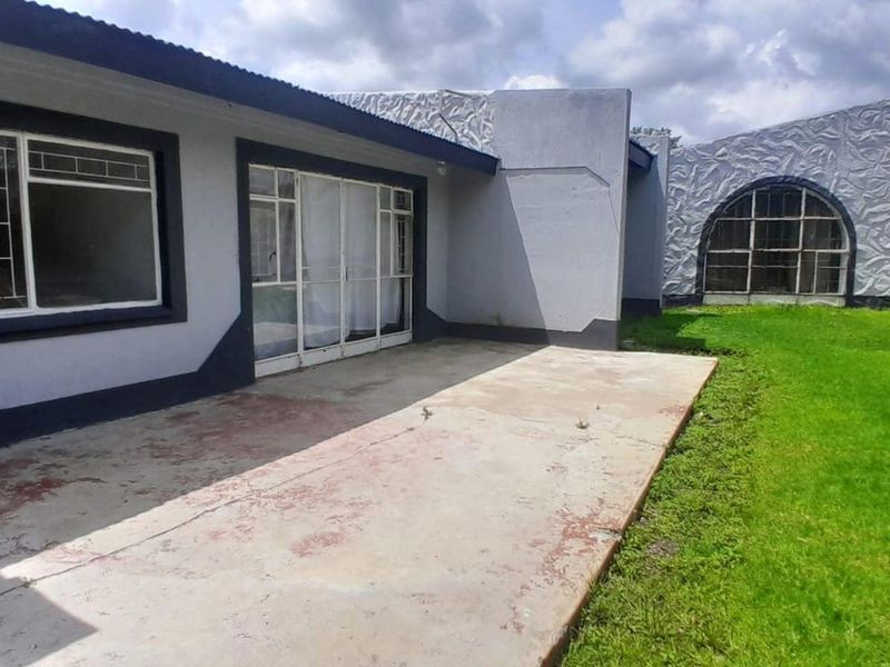 Rear exterior view featuring a concrete patio area, sliding glass doors, and unique textured wall detailing with a surrounding lawn.