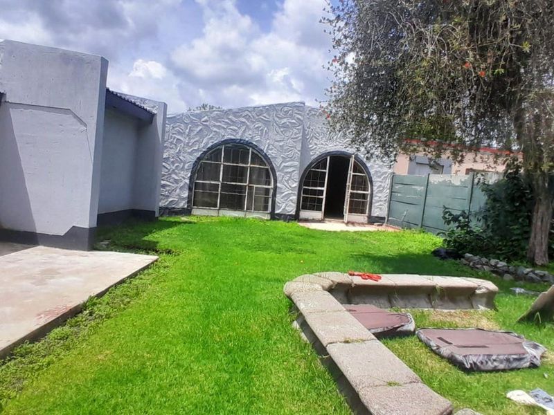 Rear view of the property featuring a textured facade with arched windows, a concrete patio area, and a garden with a stone bench.