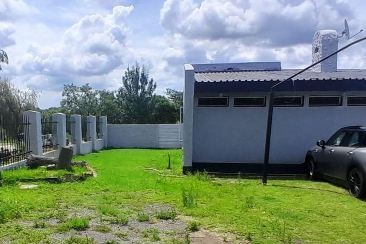 Rear exterior view of the property featuring a lawn, perimeter wall with metal fencing, and a structure with a metal roof and chimney.