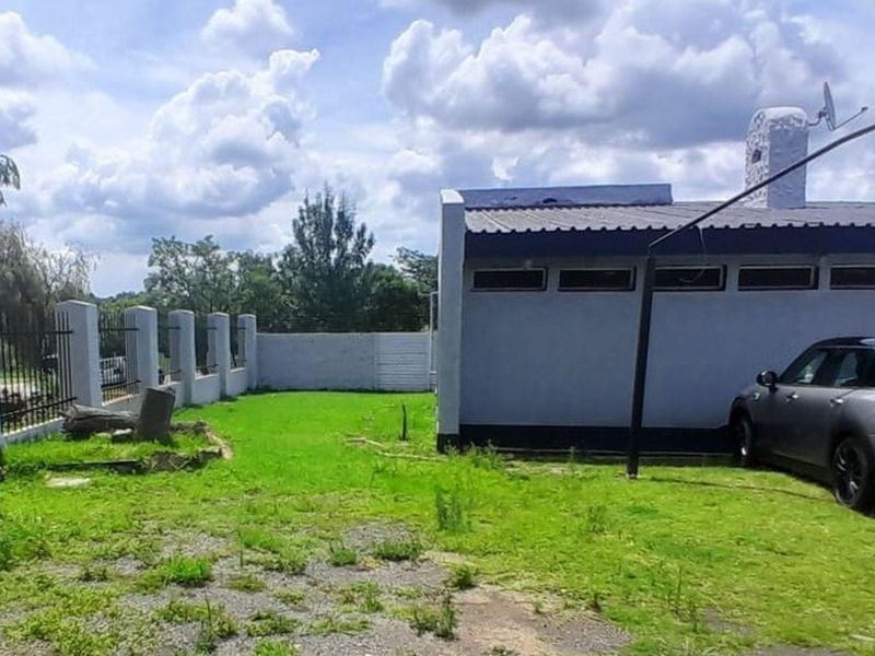 Rear exterior view of the property featuring a lawn, perimeter wall with metal fencing, and a structure with a metal roof and chimney.