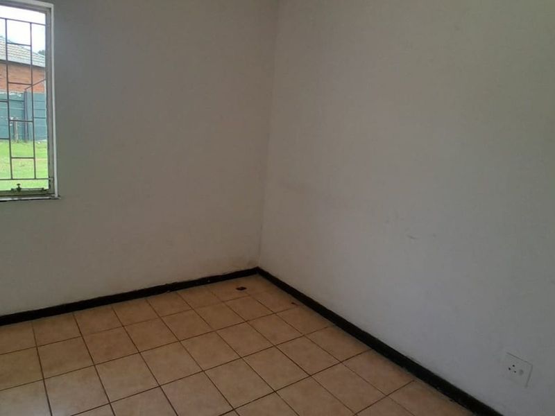 An empty bedroom featuring tiled flooring, security bars on the window, and plain white walls.