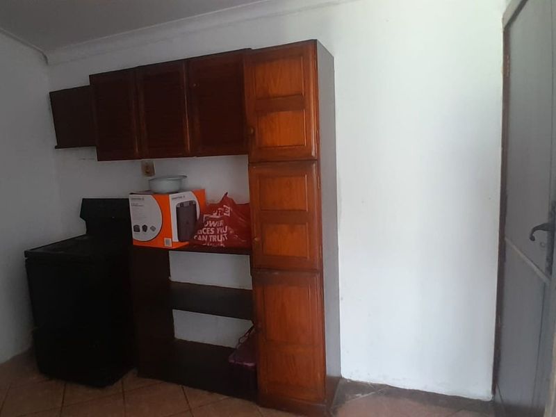 A compact kitchen area featuring dated wooden cabinetry and tiled flooring, offering potential for a modern renovation to enhance functionality and aesthetic appeal.