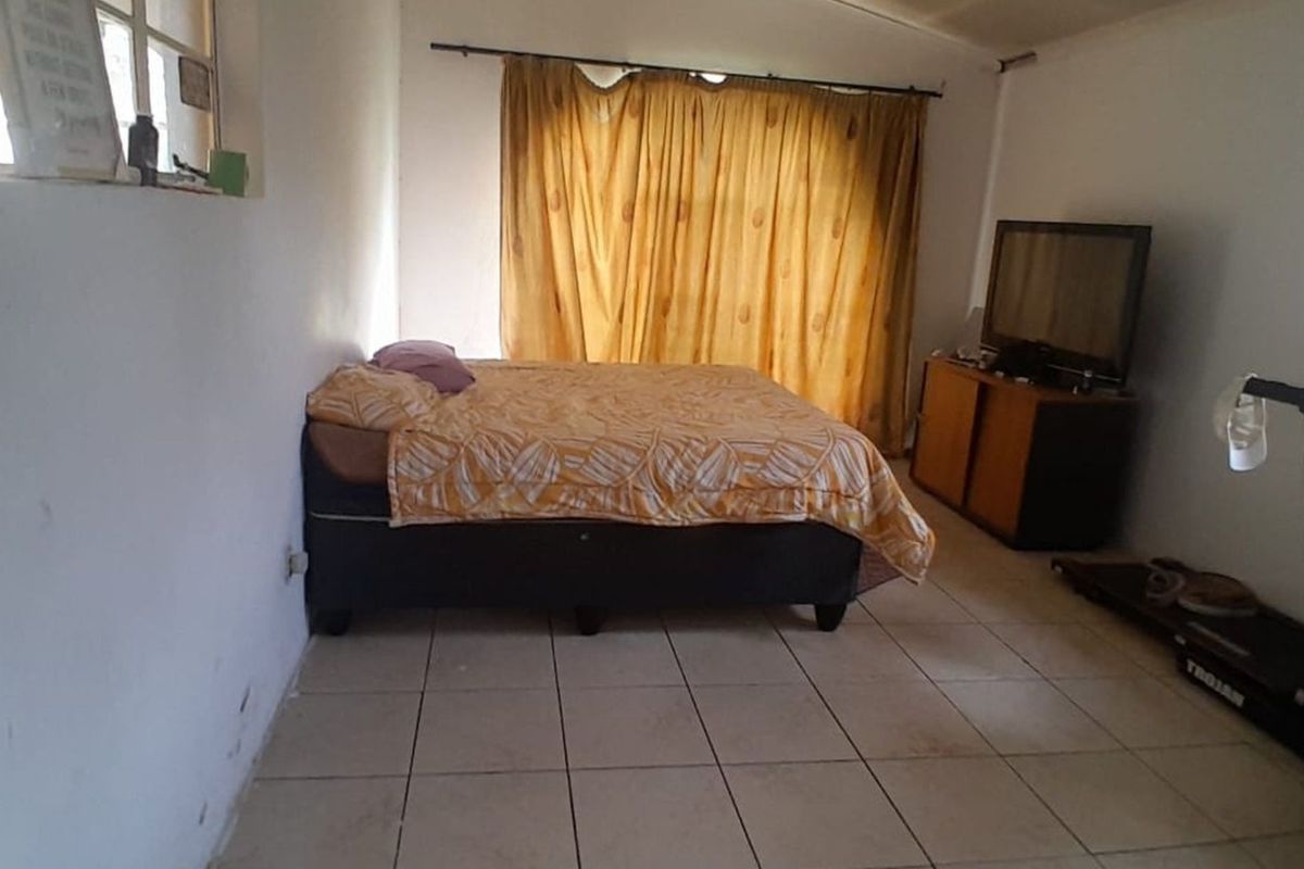 A bedroom featuring tiled flooring and a large window with curtains, offering a functional space in need of cosmetic updates.