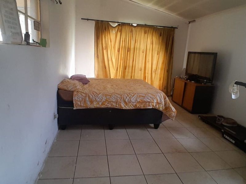 A bedroom featuring tiled flooring and a large window with curtains, offering a functional space in need of cosmetic updates.
