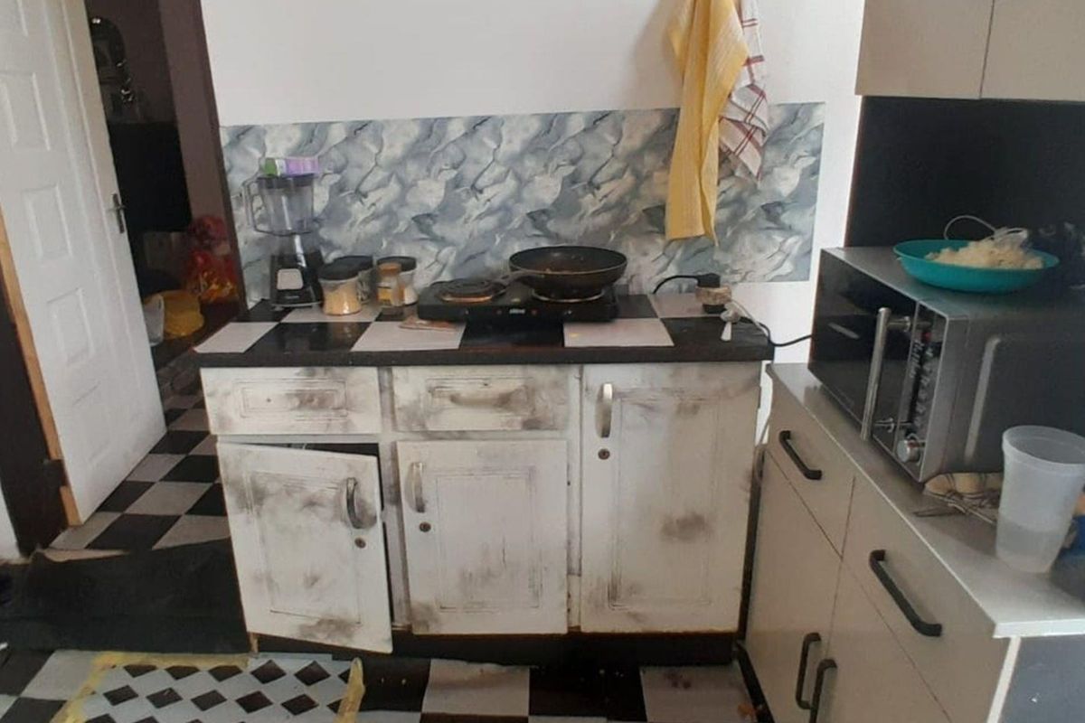 A compact kitchen area featuring built-in cabinetry, a tiled backsplash, and a microwave, currently showing significant signs of wear and requiring refurbishment.