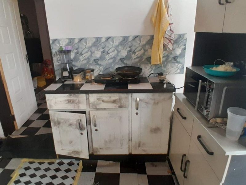 A compact kitchen area featuring built-in cabinetry, a tiled backsplash, and a microwave, currently showing significant signs of wear and requiring refurbishment.