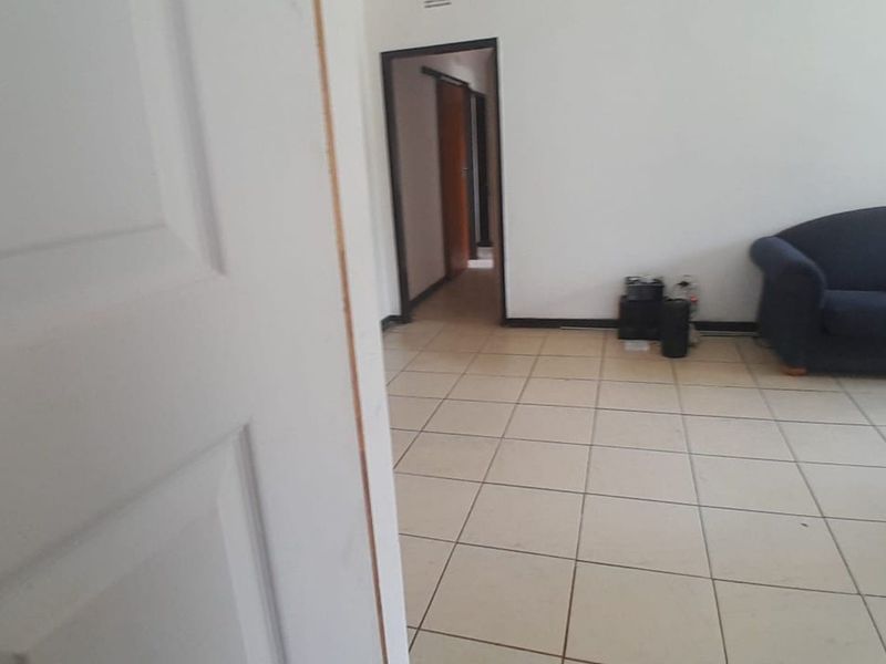 A living area featuring tiled flooring and neutral walls, leading into a hallway with internal door access.