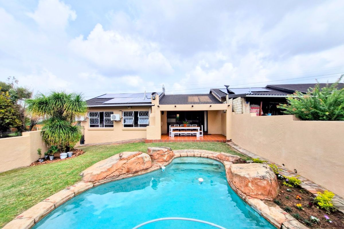 Rear view of the townhouse featuring a covered patio, a landscaped garden, and a rock-feature swimming pool with solar panels on the roof.