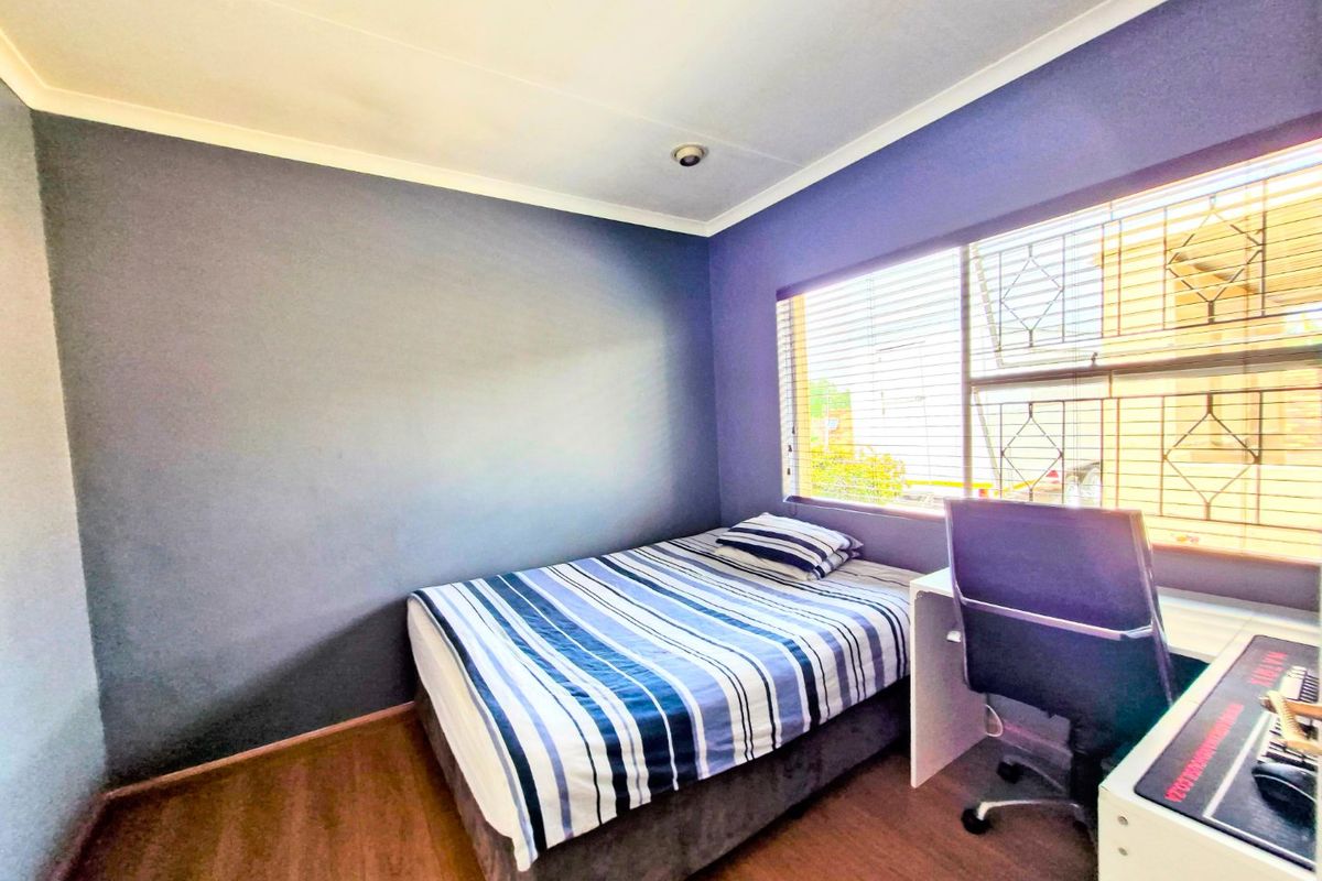 A compact bedroom featuring dark-toned walls, laminate flooring, and a window fitted with security bars and blinds.
