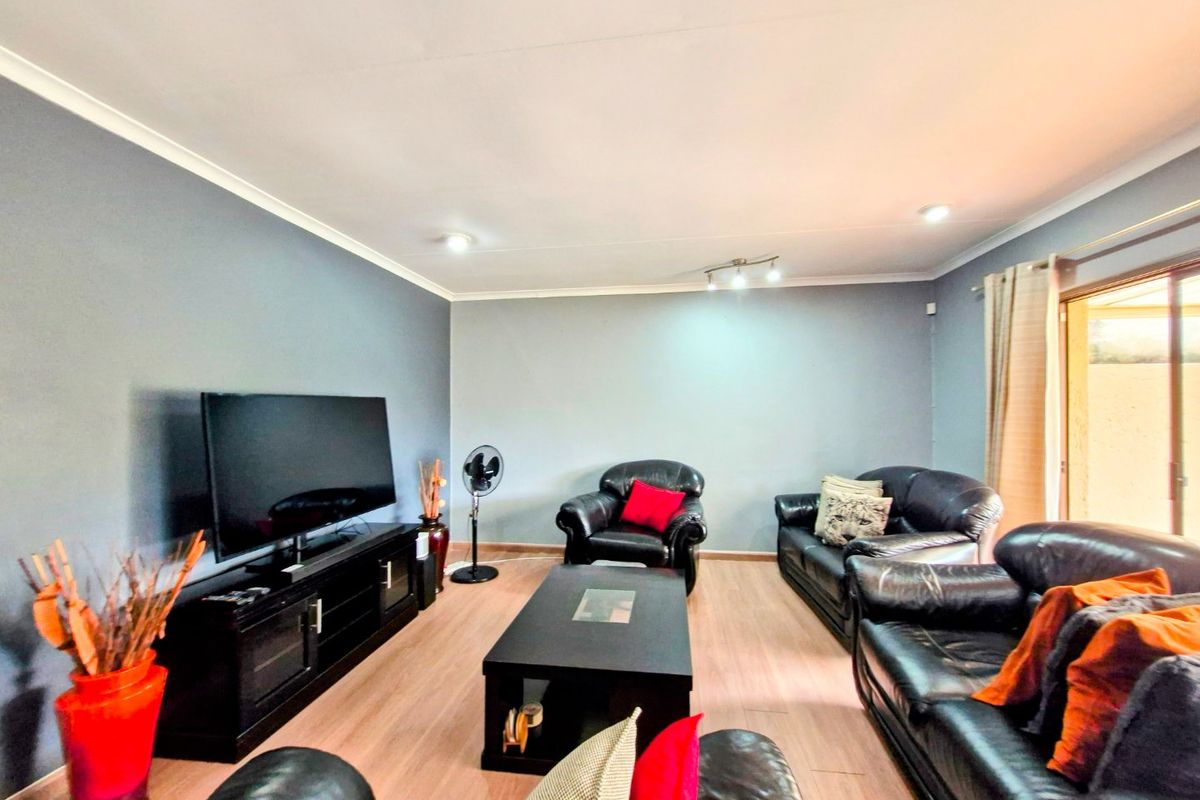 A spacious living room featuring light wood-look flooring, recessed ceiling lighting, and a sliding glass door providing access to the outdoor area.