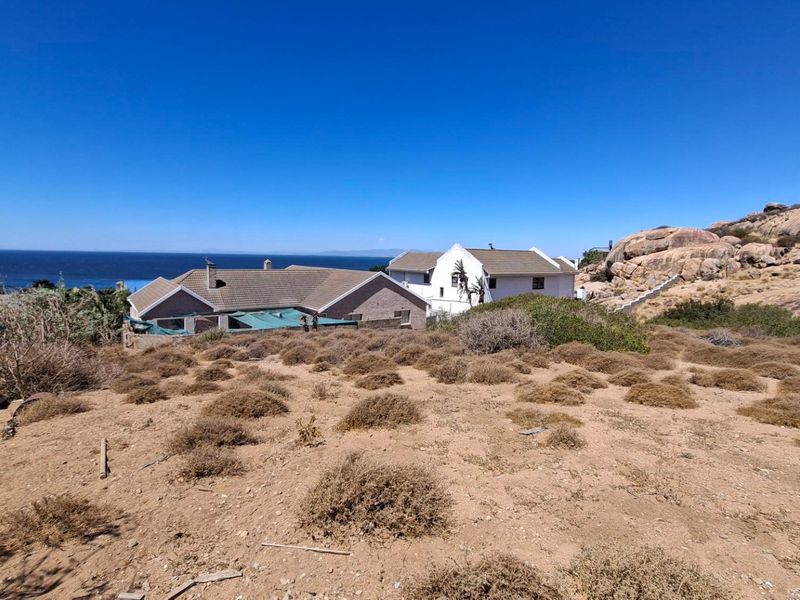 A wide-angle view of the vacant residential plot featuring natural rocky terrain and coastal scenery with neighboring properties in the background.