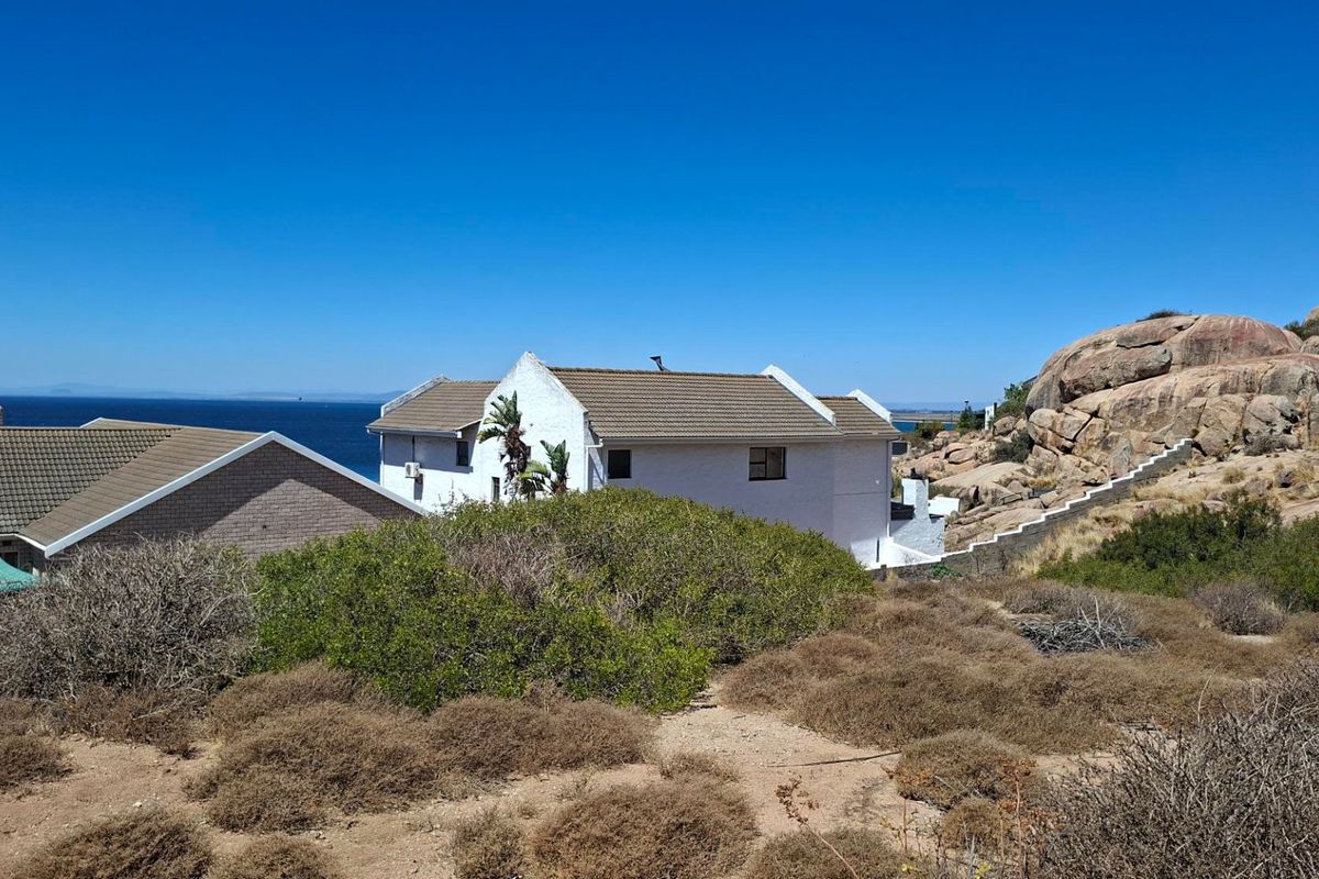 A view of the rear elevation of a coastal property featuring a tiled roof, white exterior walls, and a stone staircase set against a rocky landscape.