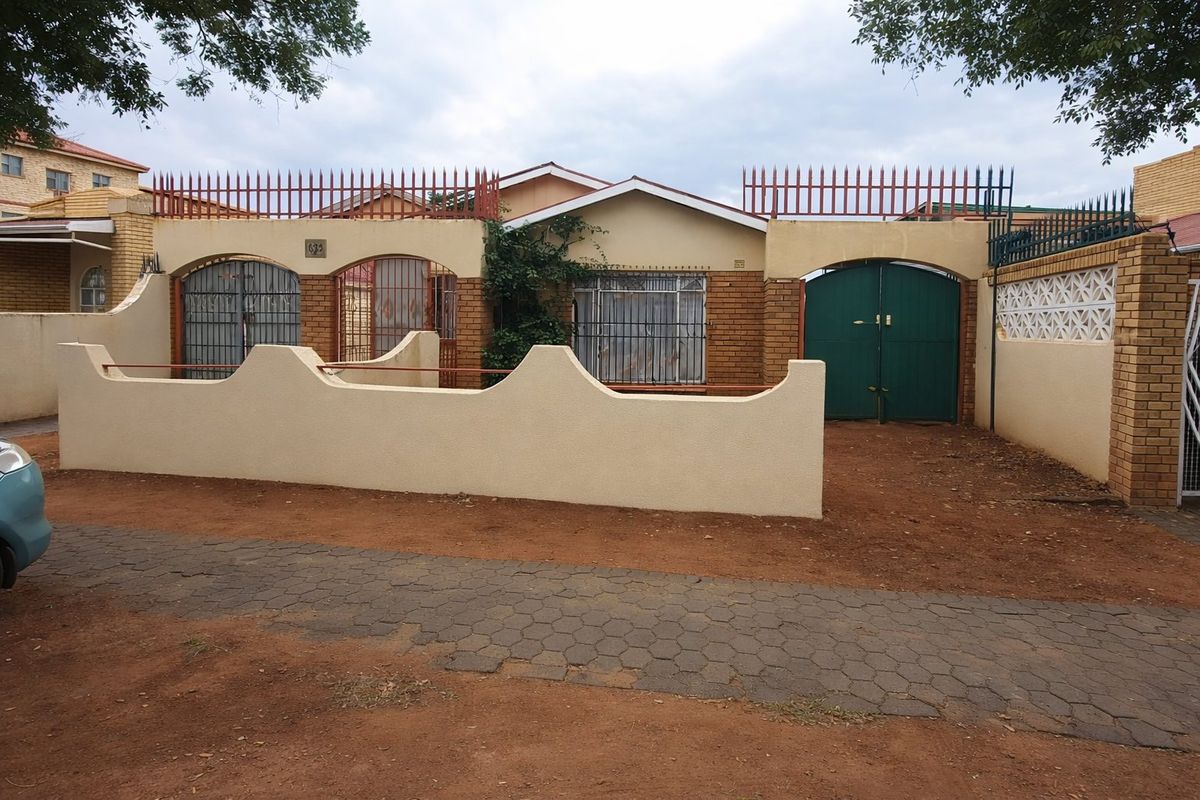 Front elevation of a residential property featuring a perimeter wall, security gates, and brick facade with security bars on windows.
