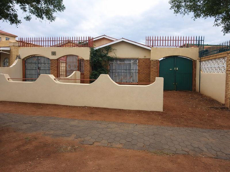 Front elevation of a residential property featuring a perimeter wall, security gates, and brick facade with security bars on windows.
