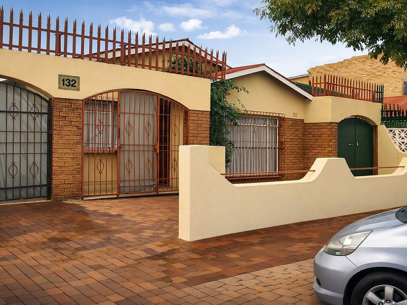 Front elevation of a residential property featuring a brick facade, secure gated entrance, and a paved driveway.