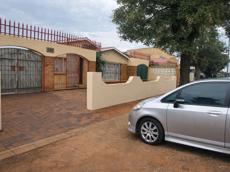 Front exterior view of the property featuring a paved driveway, brick boundary wall, and secure metal fencing and gates.