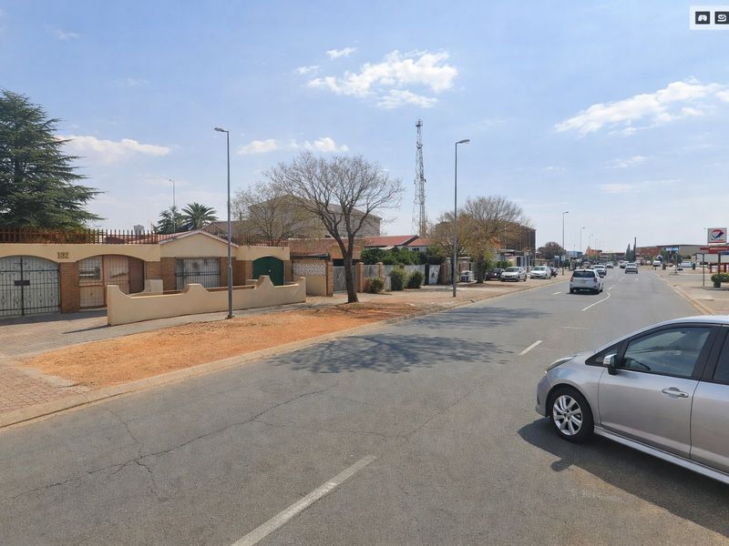 Street view showing the property frontage with boundary wall, paved driveway, and security gate access from the main road.