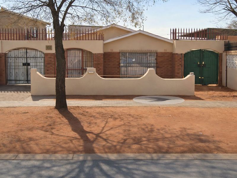 Front elevation of a single-story house featuring a brick facade, secure gated entrance, and perimeter walling with security fencing.