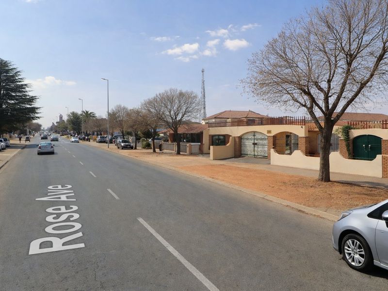 A street view of Rose Avenue showing the property's exterior boundary wall, security gate, and surrounding neighbourhood infrastructure.