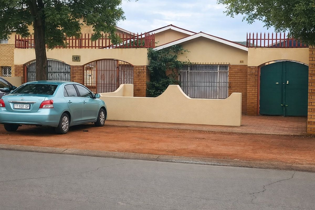 Front elevation of a single-story house featuring a brick facade, security gates, and a paved driveway area.