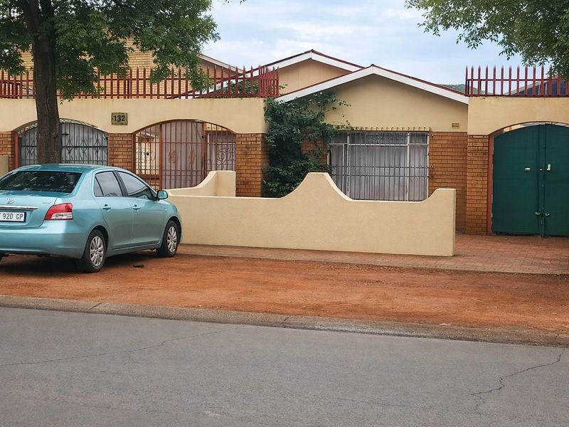 Front elevation of a single-story house featuring a brick facade, security gates, and a paved driveway area.