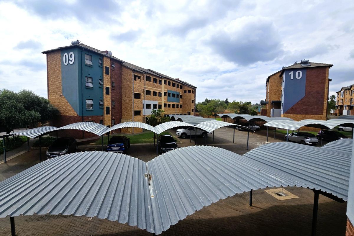 View of a residential apartment complex featuring multiple corrugated metal carports and paved parking areas between brick-clad buildings.