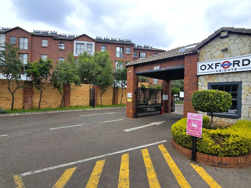 The entrance to Oxford Heights featuring a secure gated access point, brick boundary walls, and a paved driveway leading into the residential complex.