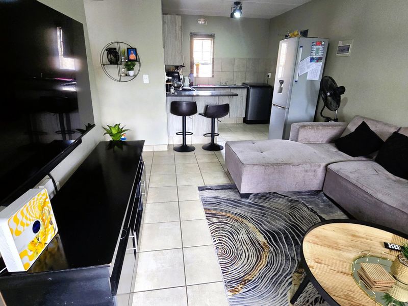 Open-plan living area featuring a combined lounge and kitchen space with tiled flooring, breakfast bar seating, and functional kitchen cabinetry.