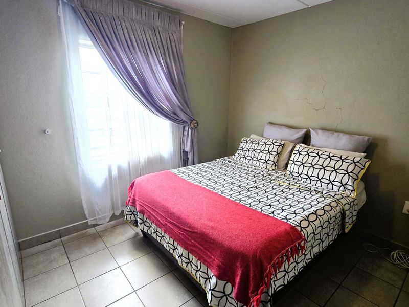 A bedroom featuring tiled flooring and a built-in wardrobe, showing visible wall plaster cracking that requires maintenance.